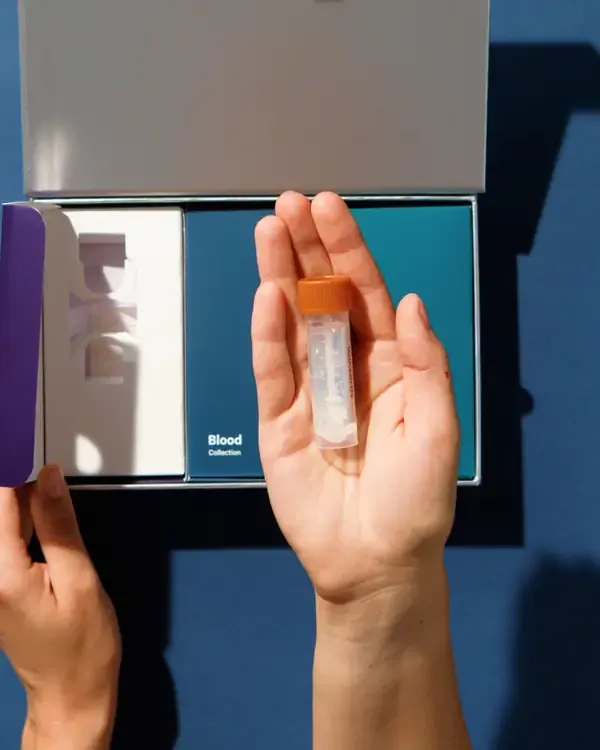 A hand holding a Viome collection tube over the open kit