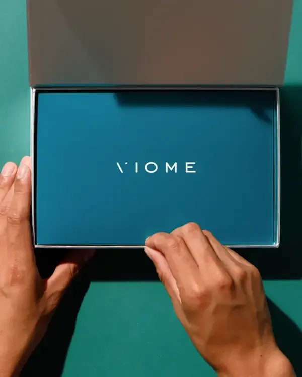 Two hands lifting the lid of a Viome kit box on a green surface